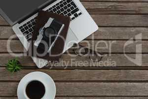Black coffee, camera, pot plant, spectacles, organizer and laptop on wooden plank