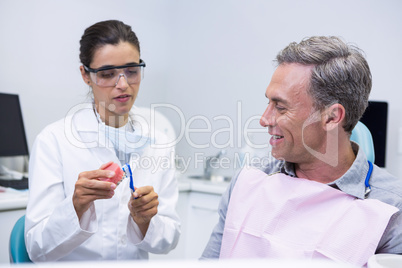 Dentist teaching man brushing teeth on dental mold