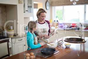 Smiling mother and daughter using digital tablet while preparing cookies