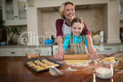 Mother and daughter rolling dough with rolling pin in kitchen