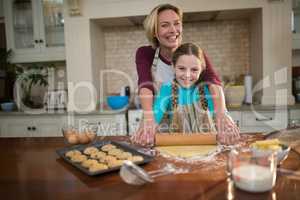 Mother and daughter rolling dough with rolling pin in kitchen