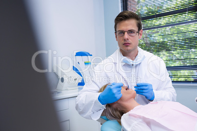 Portrait of dentist cleaning woman teeth while standing against wall