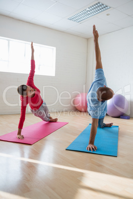 Yoga instructor with student practicing side plank pose in club