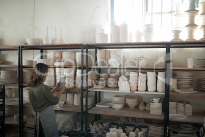 Female potter using digital tablet near shelf