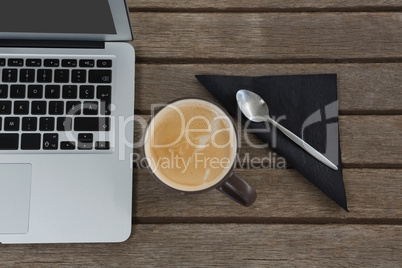 Laptop, spoon, napkin and coffee on wooden plank
