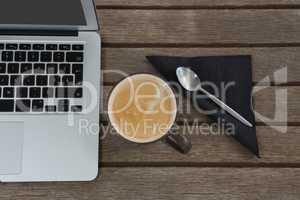 Laptop, spoon, napkin and coffee on wooden plank
