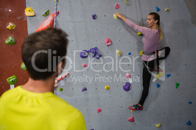 Man interacting with female athlete climbing wall in club