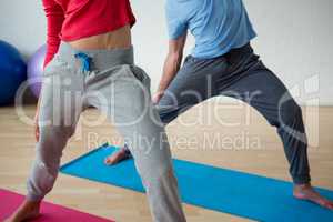 Low section of male instructor exercising with female student in club