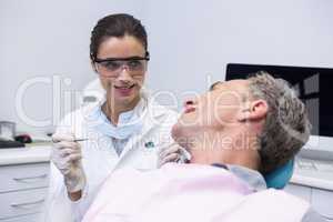 Dentist holding tool while looking at man in clinic