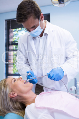 Dentist cleaning woman teeth while standing against wall