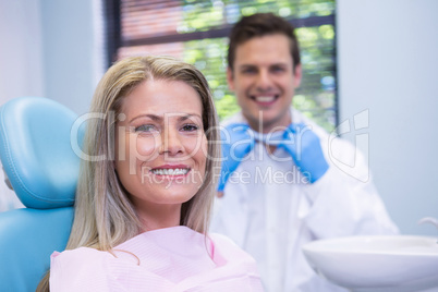 Smiling woman sitting on chair against dentist at medical clinic