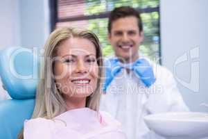 Smiling woman sitting on chair against dentist at medical clinic