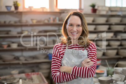 Female potter standing with arms crossed in pottery workshop