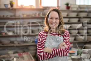 Female potter standing with arms crossed in pottery workshop