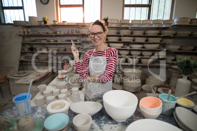 Portrait of female potter standing with mobile phone