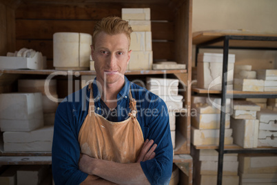 Male potter standing with arms crossed in pottery workshop