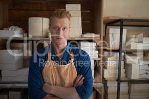 Male potter standing with arms crossed in pottery workshop