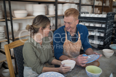Male and female potter interacting while decorating earthenware
