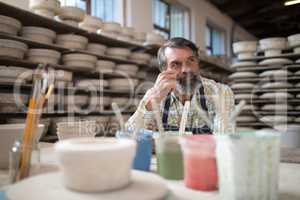 Thoughtful male potter sitting at worktop