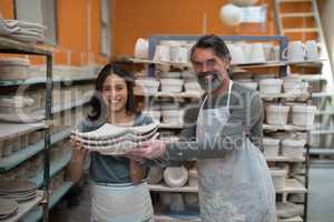 Portrait of male and female potter holding ceramic plates