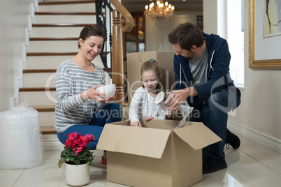 Parents and daughter opening cardboard boxes in living room