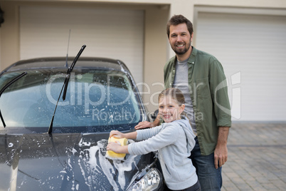 Teenage girl and father washing a car on a sunny day