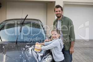 Teenage girl and father washing a car on a sunny day