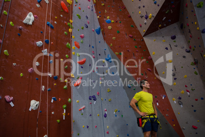 Male athlete with hands on hip standing by climbing wall