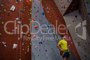 Male athlete with hands on hip standing by climbing wall