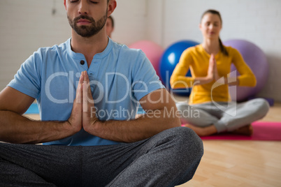 Yoga instructor with student meditating in prayer position at club