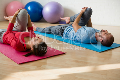 Yoga instructor and student exercising while lying on mat in health club