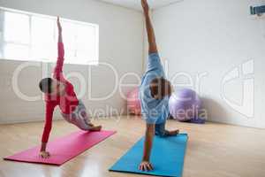 Male instructor with student practicing side plank pose in yoga studio