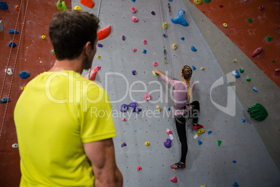 Rear view of man looking at female athlete climbing wall