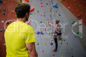 Rear view of man looking at female athlete climbing wall