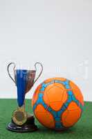 Football, trophy and medal on artificial grass against white background