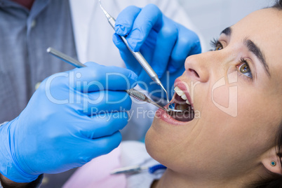 Dentist holding tools while examining woman at clinic