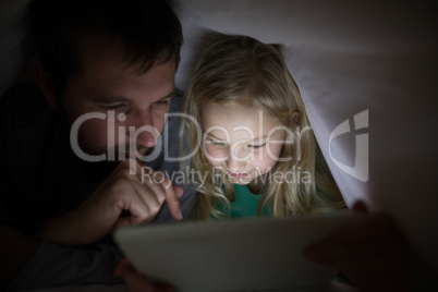 Father and daughter lying under blanket and using digital tablet