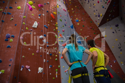 Athletes with hands on hip standing by climbing wall in gym Athletes with hands on hip standing by climbing wall in gym
