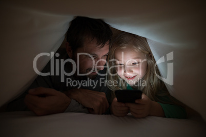 Father and daughter lying under blanket and using mobilephone