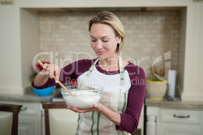 Smiling woman mixing eggs and wheat flour