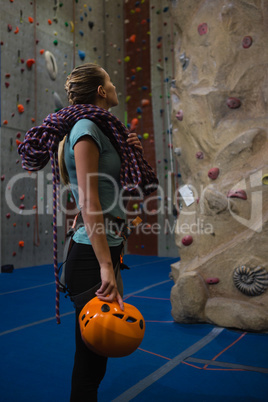 Athlete with rope and sports helmet looking at climbing wall in club