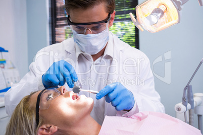 Dentist holding tools while examining woman