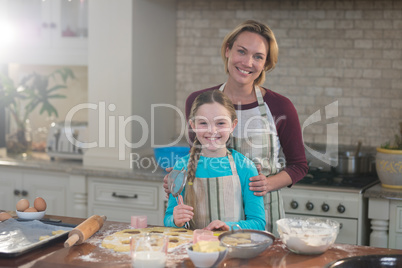 Smiling mother and daughter preparing cookies in kitchen