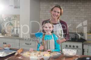 Smiling mother and daughter preparing cookies in kitchen