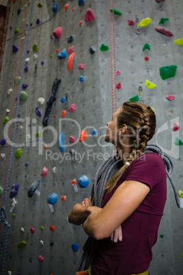 Athlete with rope looking up while standing by climbing wall in club
