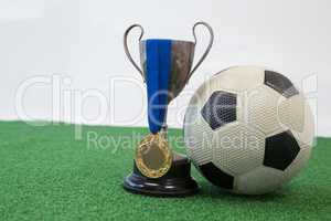 Football, trophy and medal on artificial grass against white background