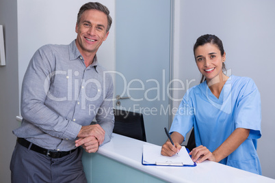 Portrait of smiling doctor holding pen standing by man at desk