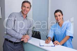 Portrait of smiling doctor holding pen standing by man at desk