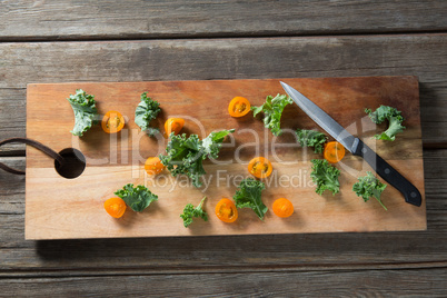 Kale with tomato slices on cutting board with knife at table