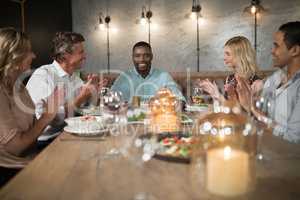 Group of happy friends applauding man while dining